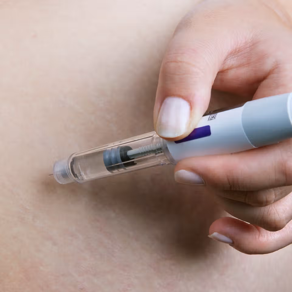 Close-up of a hand using an insulin pen to inject medication subcutaneously into the skin.