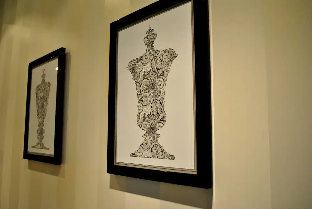 Two framed black and white illustrations of ornate vases hang on a cream-colored wall with subtle vertical stripes.