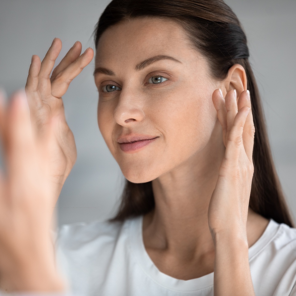 Close up beautiful woman looking in mirror in bathroom, touching face, pretty young female checking makeup, satisfied by healthy perfect skin, natural beauty concept, face care and treatment