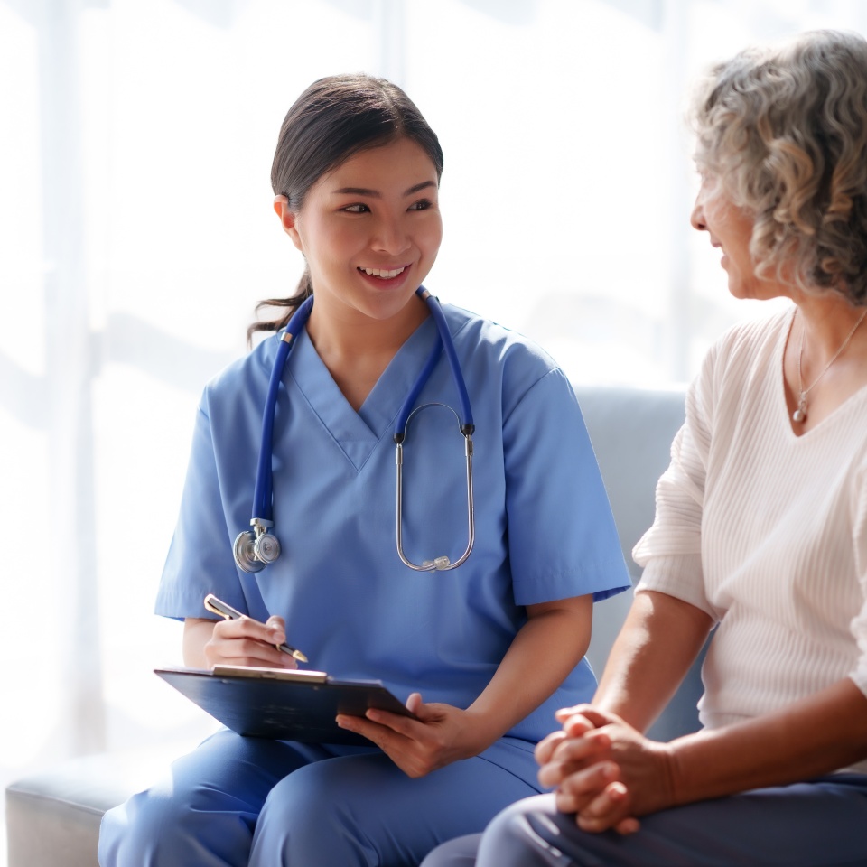 Asian female doctor or nurse gently guide and care for elderly patient at home, giving warm encouragement and consolation.