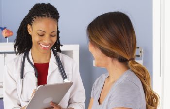 Black doctor with tablet talking to female Asian patient